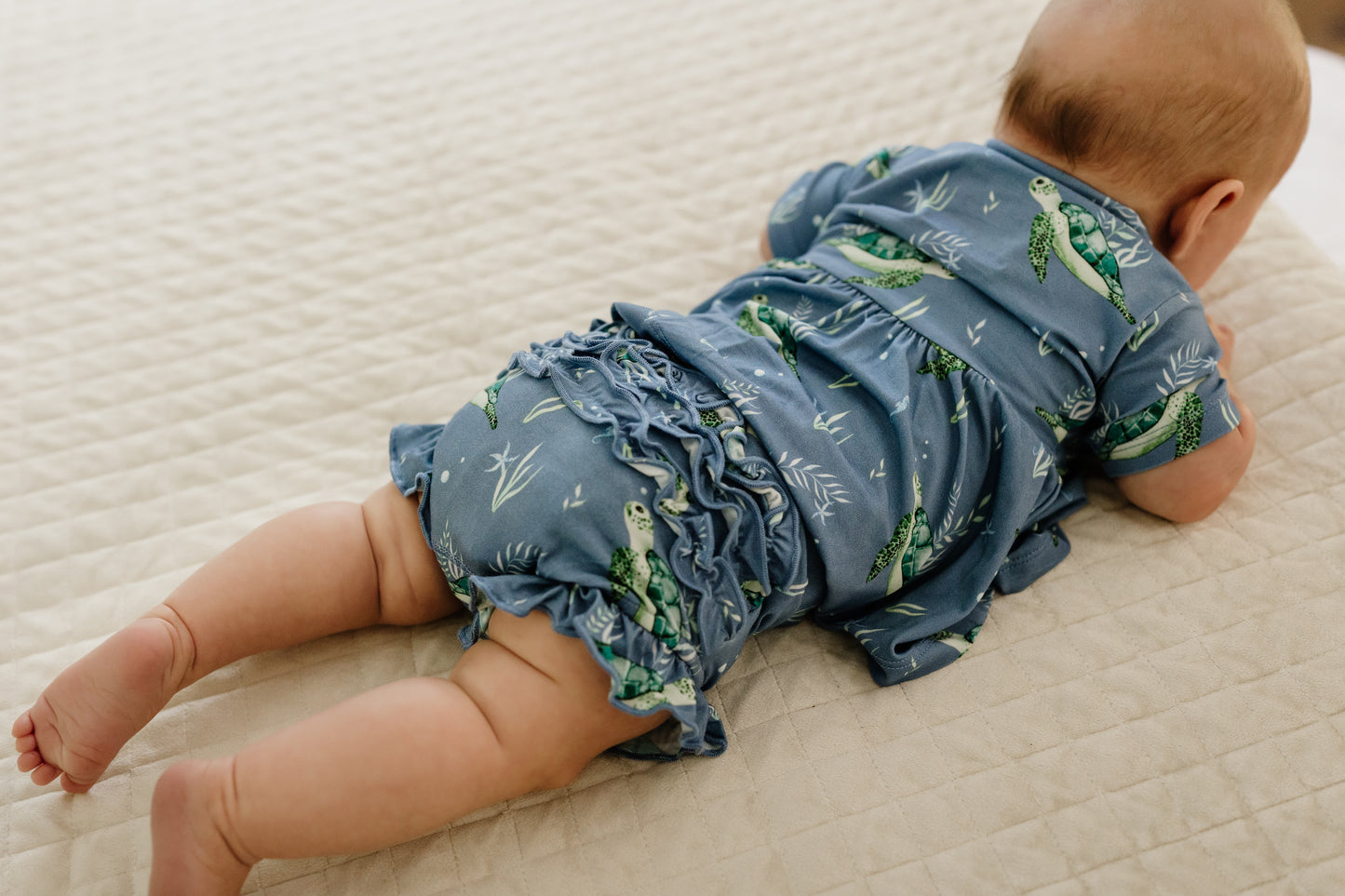 Infant laying on belly on bead wearing peplum and ruffle bloomers set