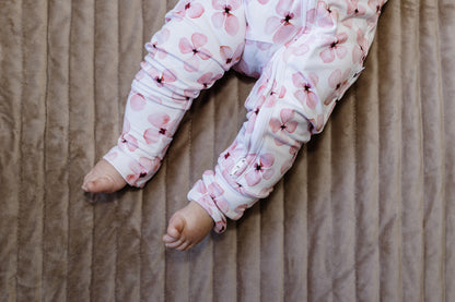 Baby legs wearing pink floral pajama zippy on a beige blanket