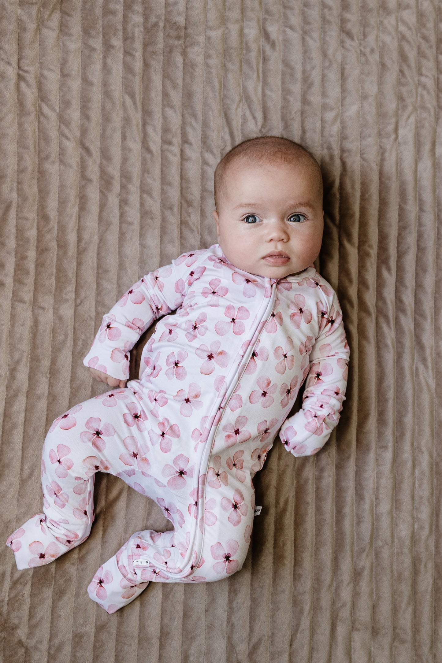 Baby in a pink floral onesie lying on a textured surface