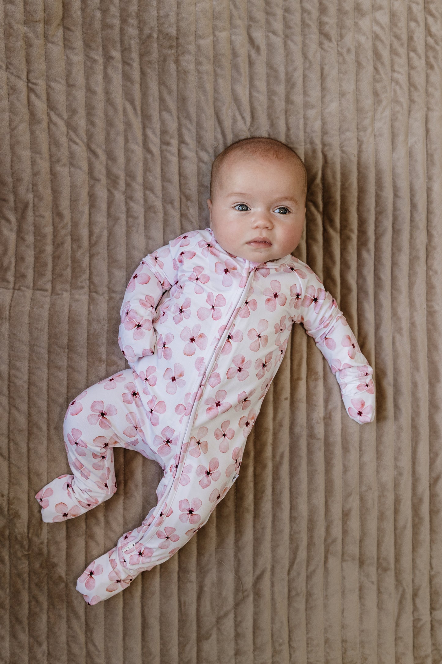 Baby in a floral onesie lying on a textured brown surface