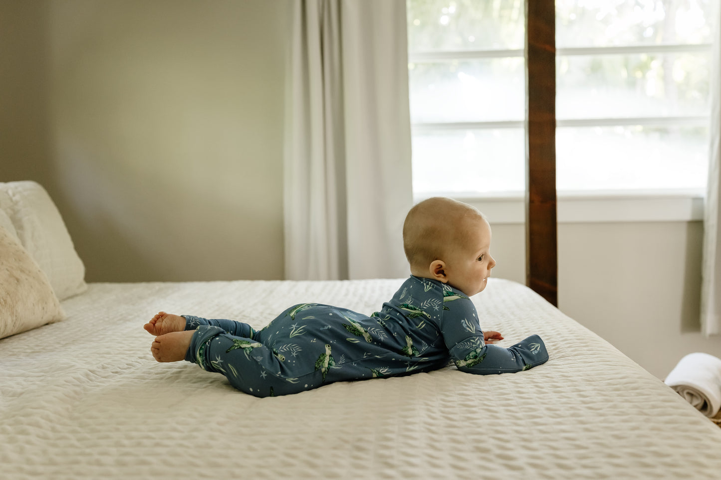 Baby lying on a bed wearing blue sea turtle zippy pajamas 