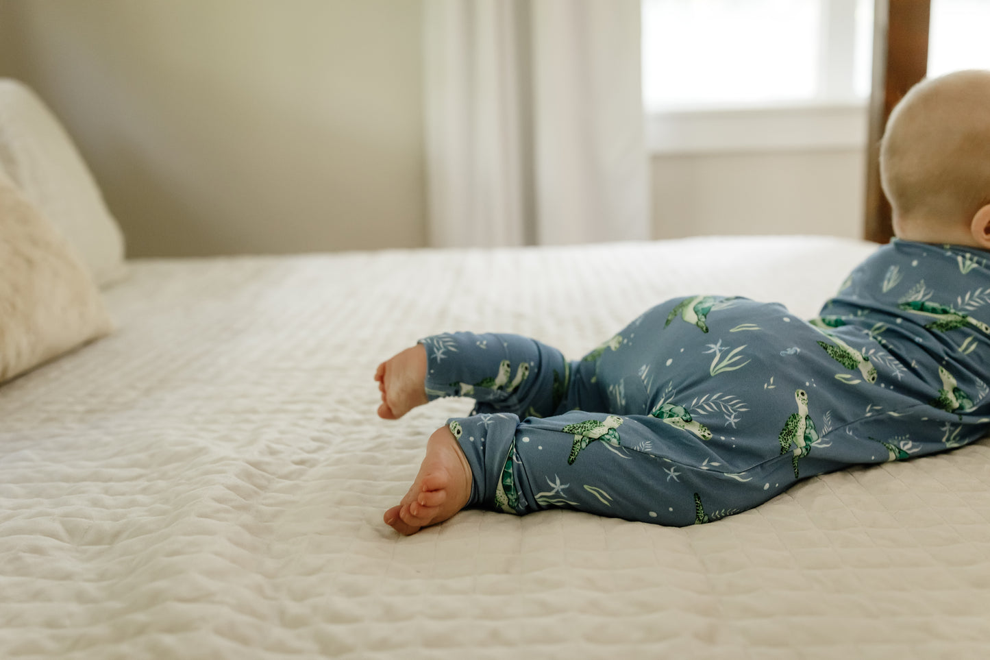 Baby lying on a bed wearing blue sea turtle zippy pajamas 