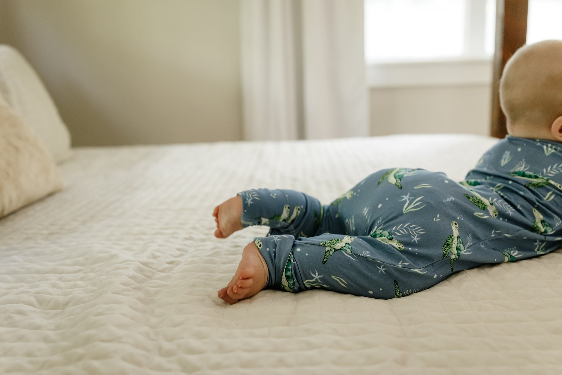 Baby lying on a bed wearing blue sea turtle zippy pajamas 