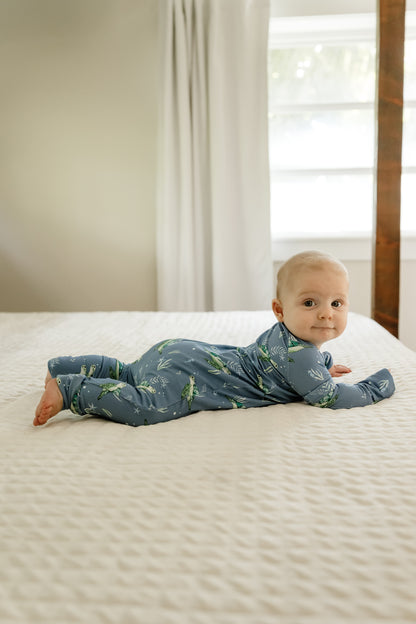 Baby lying on a textured mattress in a softly lit room wearing the sea turtle zippy pajamas 