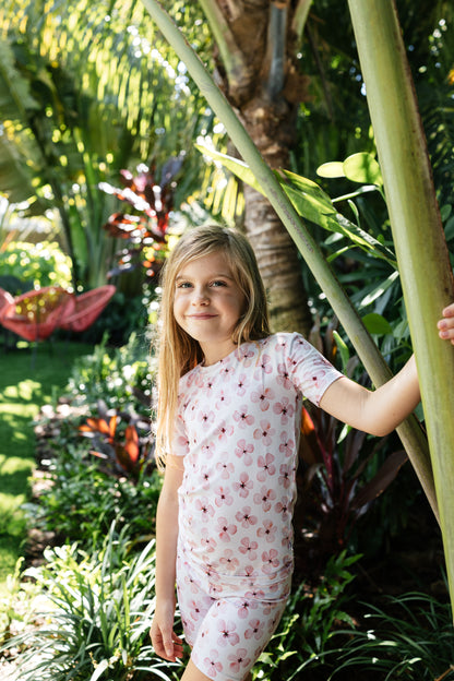 Seven-year-old girl with a tropical background wearing white short sleeve pajamas with pink flowers