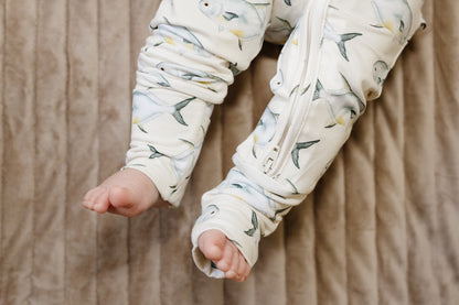 Baby's legs in a permit fish patterned onesie on a beige blanket