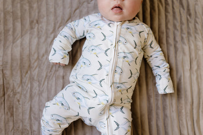 Baby wearing a yellow zippy onesie with permit fish pattern on a beige background