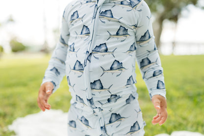 A person outdoors wearing a light blue long-sleeve zip-front top with a repeating sailfish print in dark blue and gray, standing on a grassy lawn.