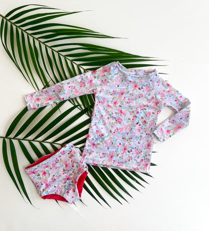 Floral long-sleeve shirt and reversible swim bottoms set on a white background with palm leaves.