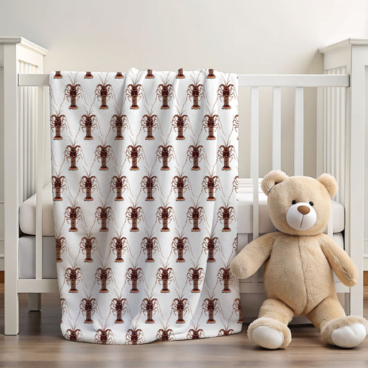 A white baby blanket featuring a repeating brown lobster pattern, draped over a white wooden crib next to a beige teddy bear in a nursery setting.