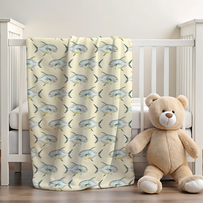 Crib with a permit fish-patterned blanket and a teddy bear on a wooden floor.