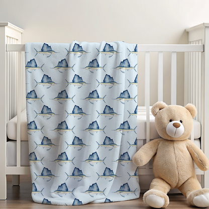 Crib with a sailfish fish-patterned blanket and a teddy bear on a light wooden floor.