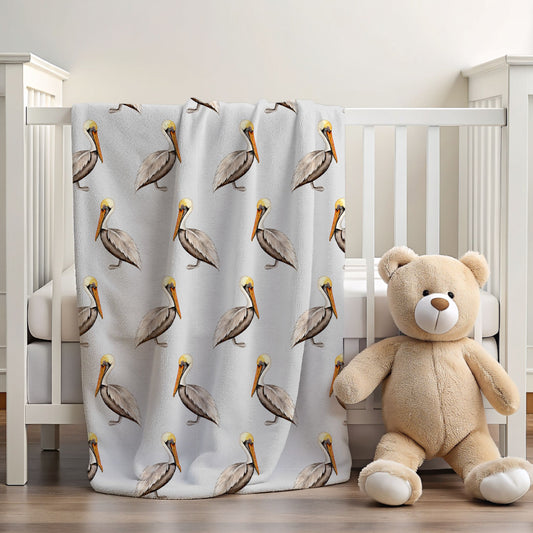 A white crib in a nursery setting with a light gray blanket featuring a repeating pattern of brown pelicans with yellow beaks and heads. A beige teddy bear plush toy sits on the floor next to the crib.